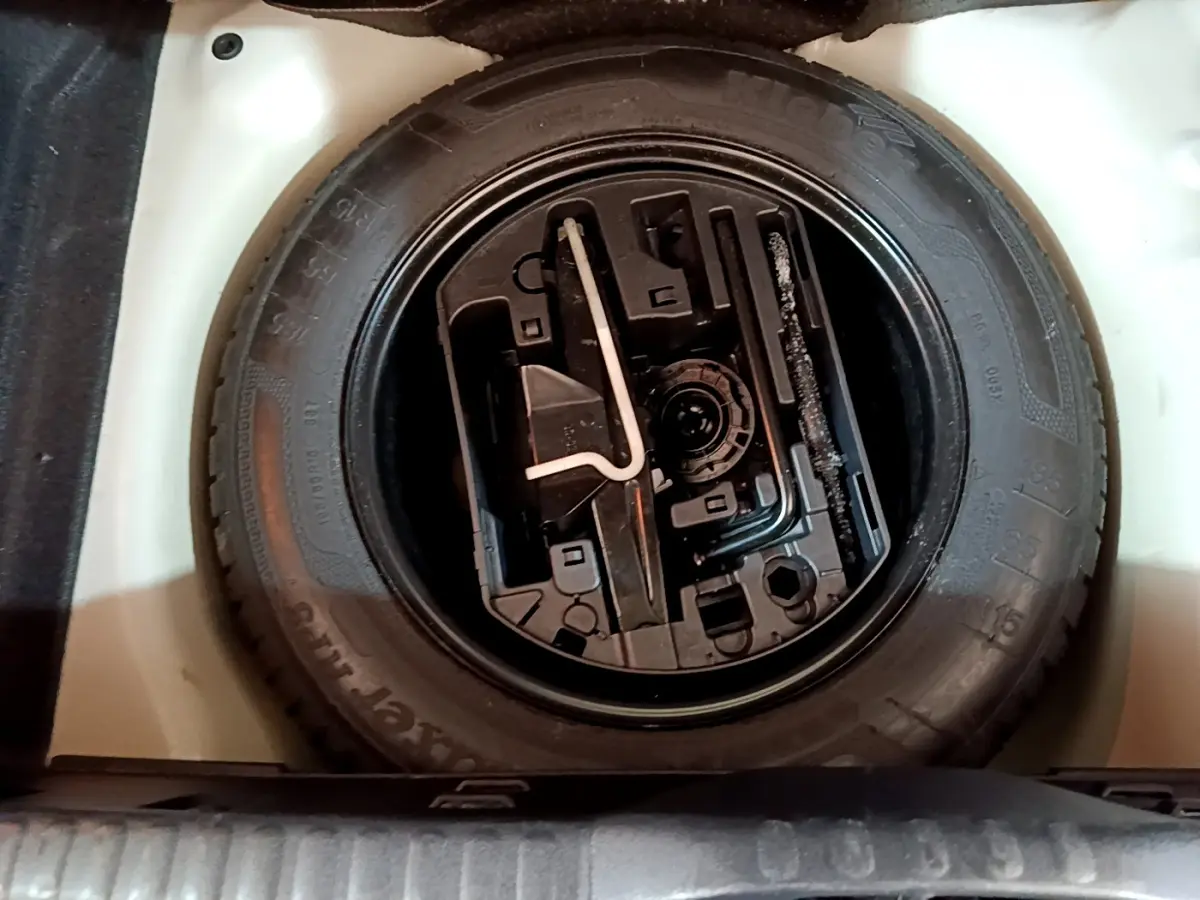 Vue plongeante sur la roue de secours noire et ses outils dans le coffre blanc d'une Citroën C3 2019 PureTech.