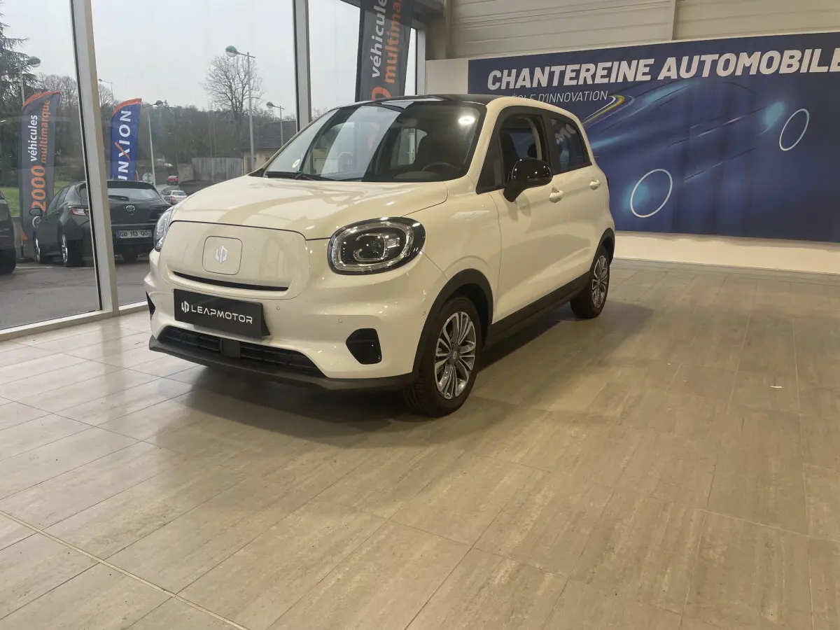 Vue 3/4 avant droite d'une Leapmotor T03 Luxury blanche électrique en showroom avec détails noirs contrastants.