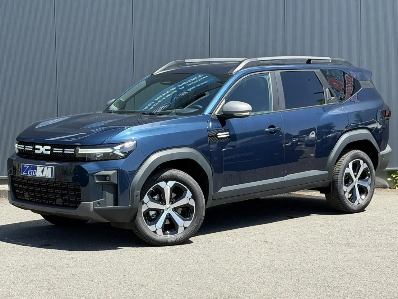 SUV Dacia Bigster bleu indigo en 3/4 avant droit avec barres de toit et jantes alliage diamantées.