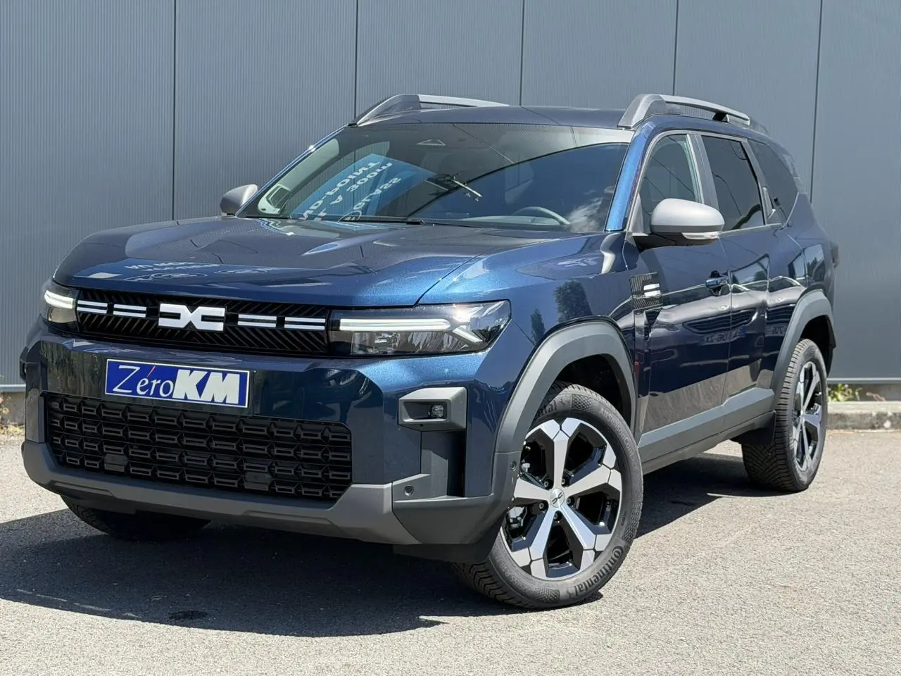 SUV Dacia Bigster bleu indigo en 3/4 avant droit avec jantes alliage et barres de toit gris mégalithe.