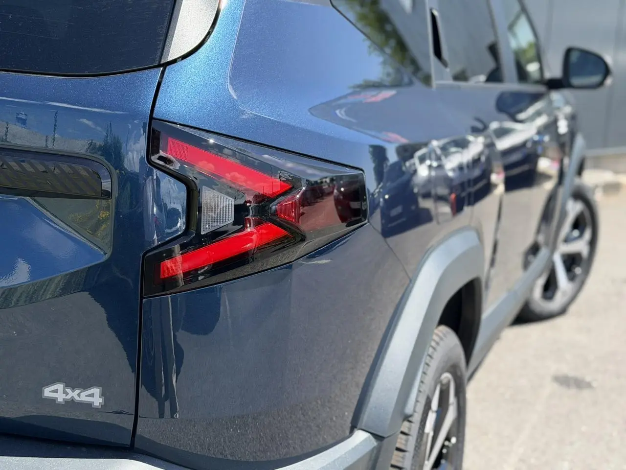 Vue 3/4 arrière droite du Dacia Bigster bleu indigo avec feux arrière en forme de flèche et logo 4x4 visible.