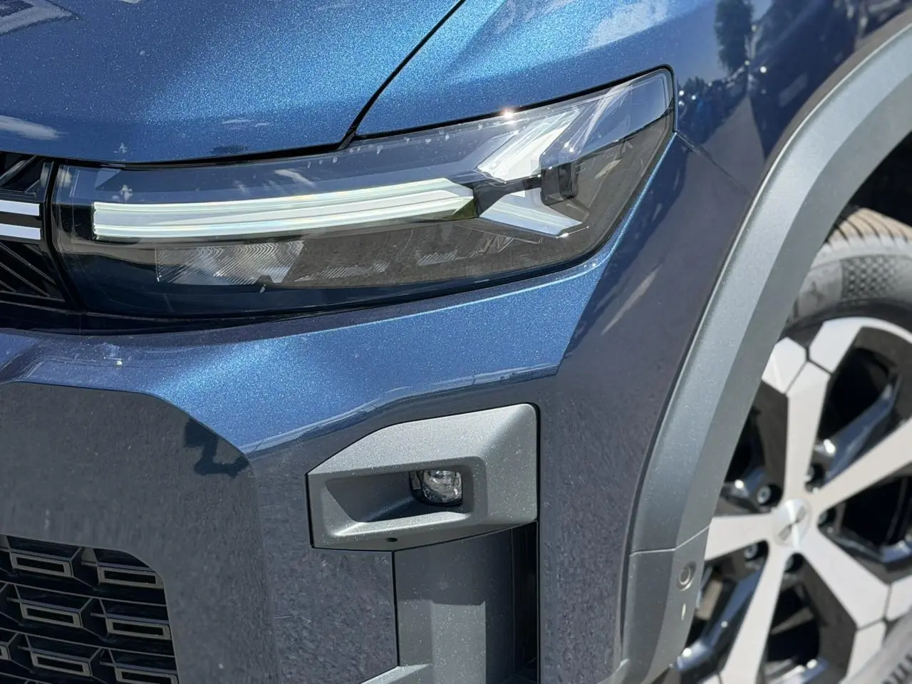 Gros plan sur l'avant droit bleu indigo du Dacia Bigster Hybrid-G 150, mettant en valeur le phare LED et la jante alliage 18 pouces.