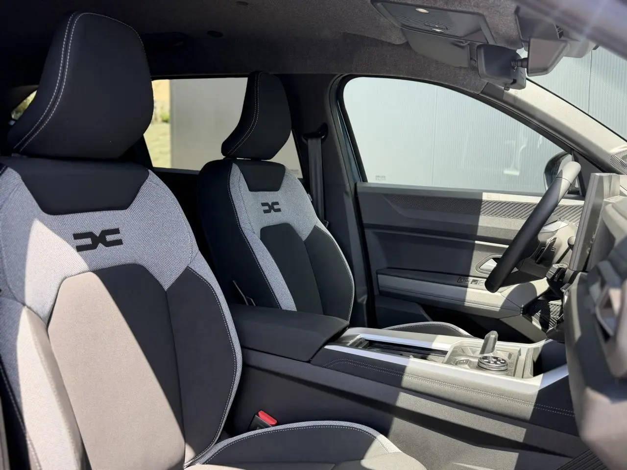Vue intérieure côté droit du DACIA BIGSTER 2026, sièges avant bicolores avec logo DC, volant et console centrale visibles.