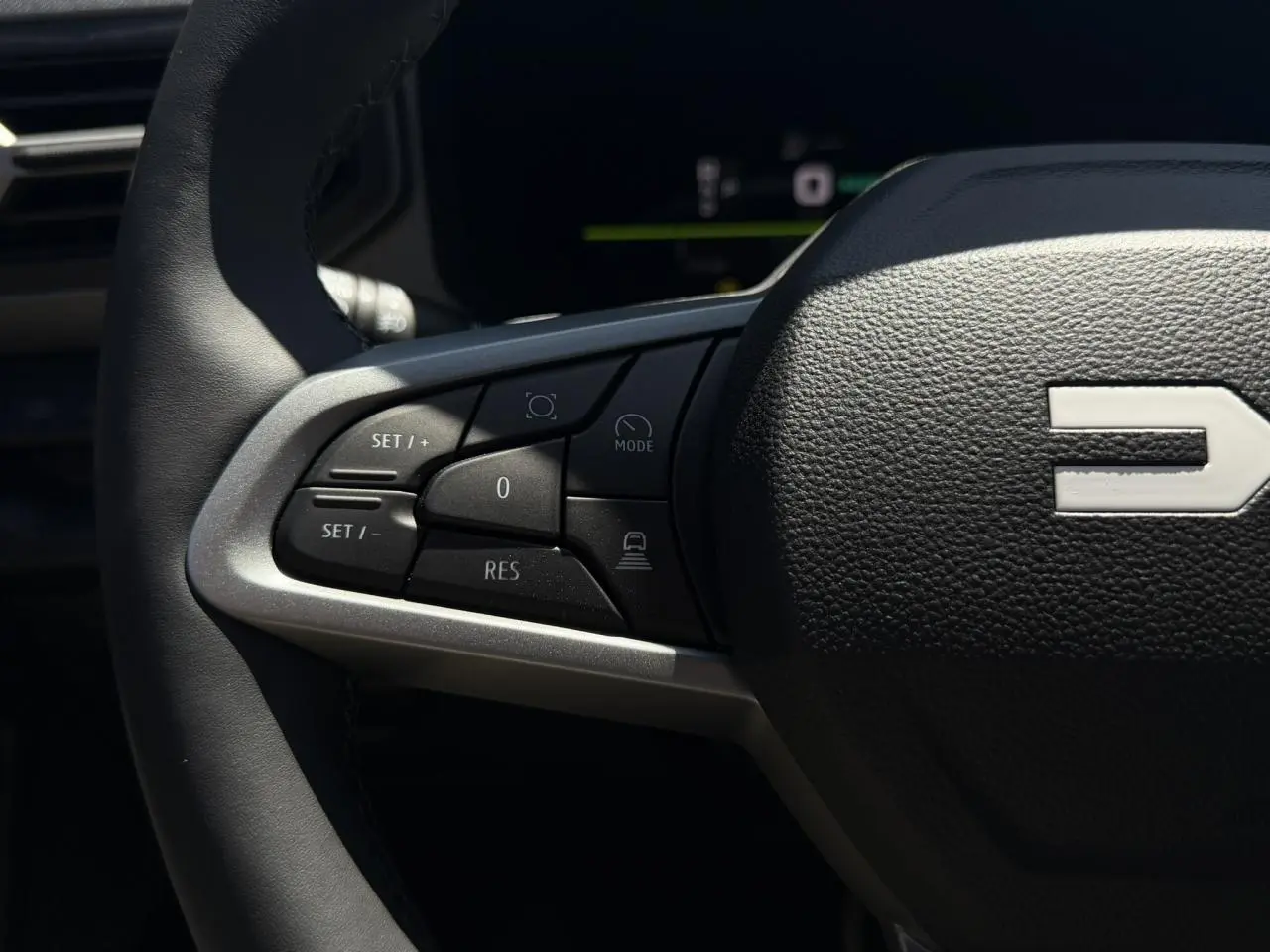 Gros plan sur les commandes à gauche du volant noir du Dacia Bigster Hybrid-G 150 4x4, avec logo Dacia visible.