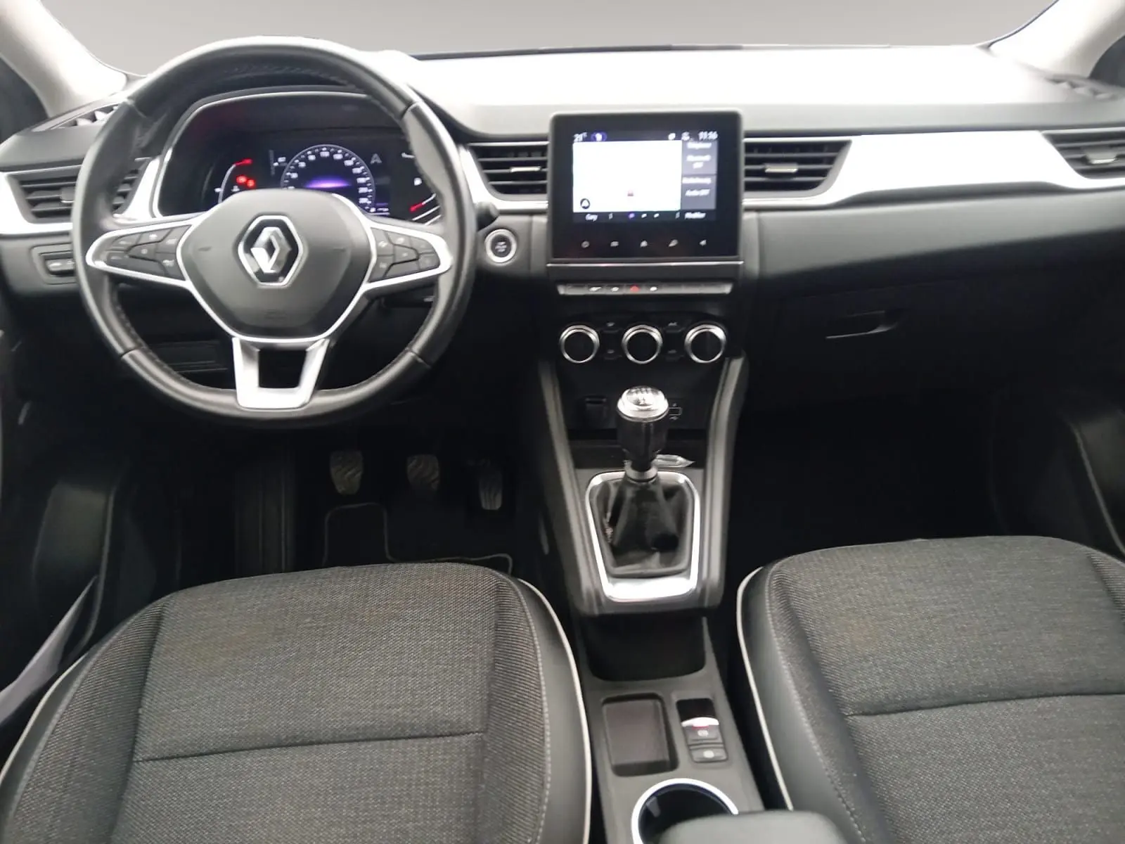 Vue intérieure frontale du tableau de bord du Renault Captur 2023 avec volant multifonction, écran tactile et levier de vitesse manuel.