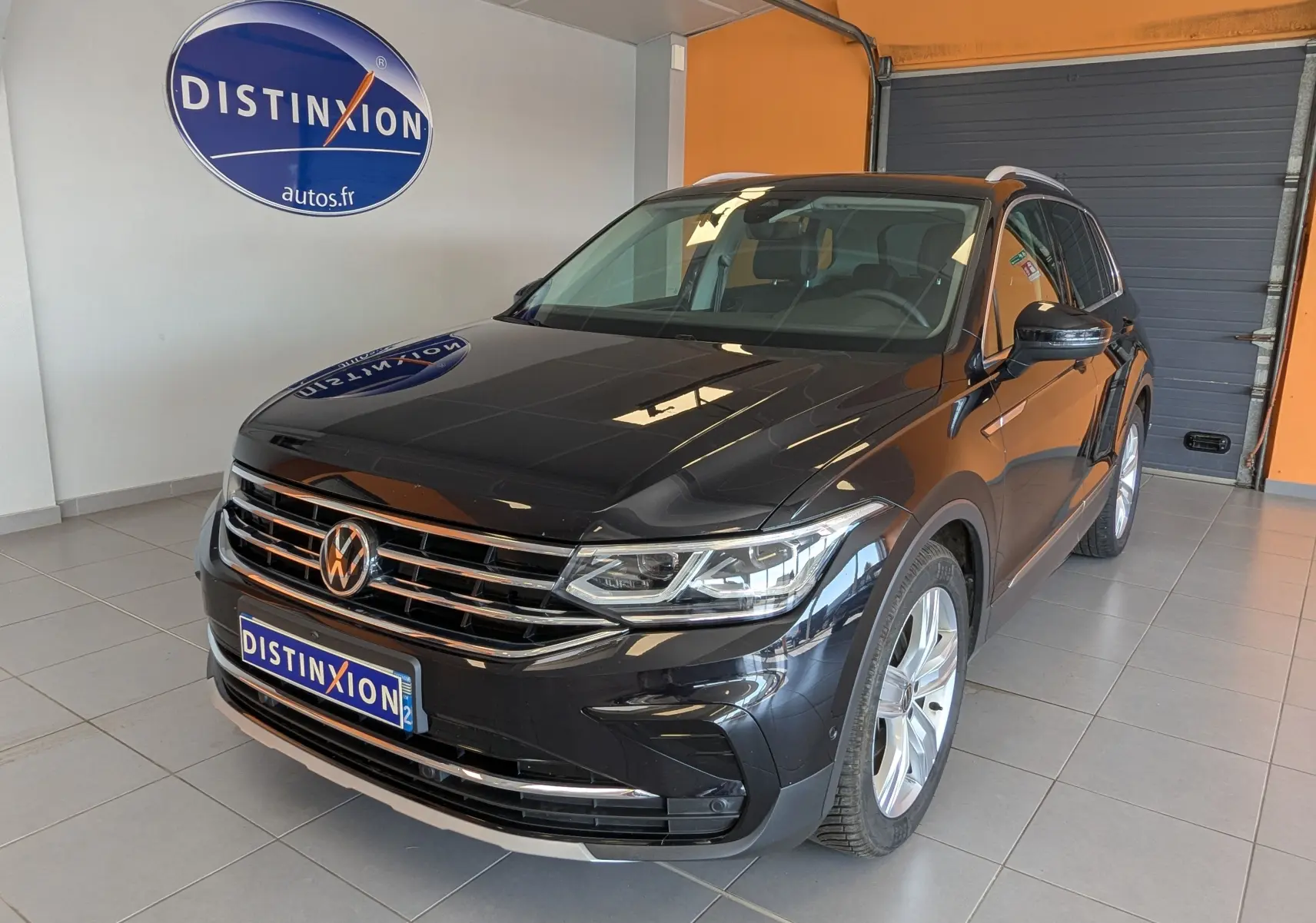 Volkswagen Tiguan noir 2.0 TDI 150ch vue 3/4 avant droit en intérieur avec logo Distinxion en arrière-plan.