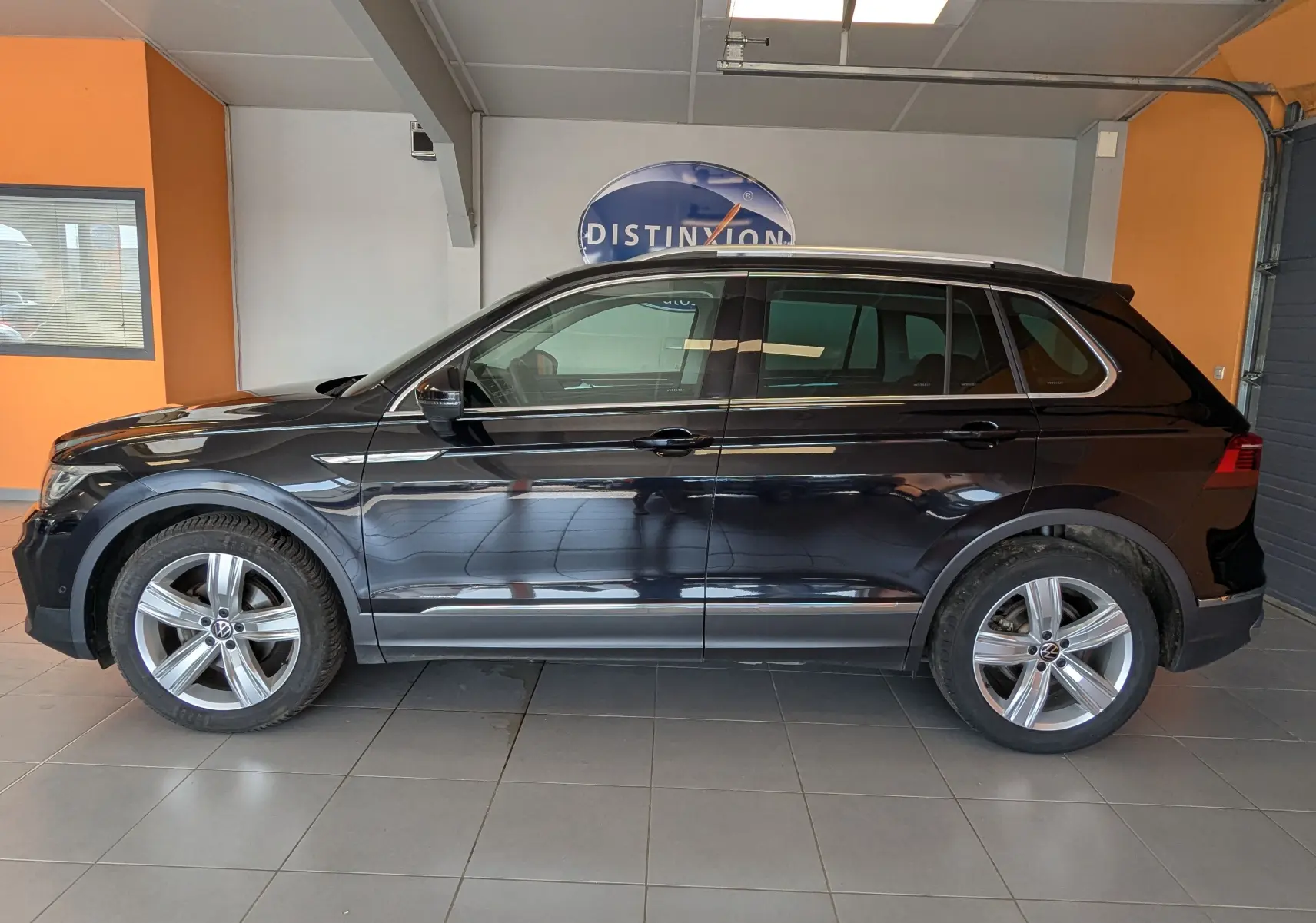Vue de profil côté gauche d'un Volkswagen Tiguan noir 2021 dans un showroom avec jantes alliage et vitres teintées.