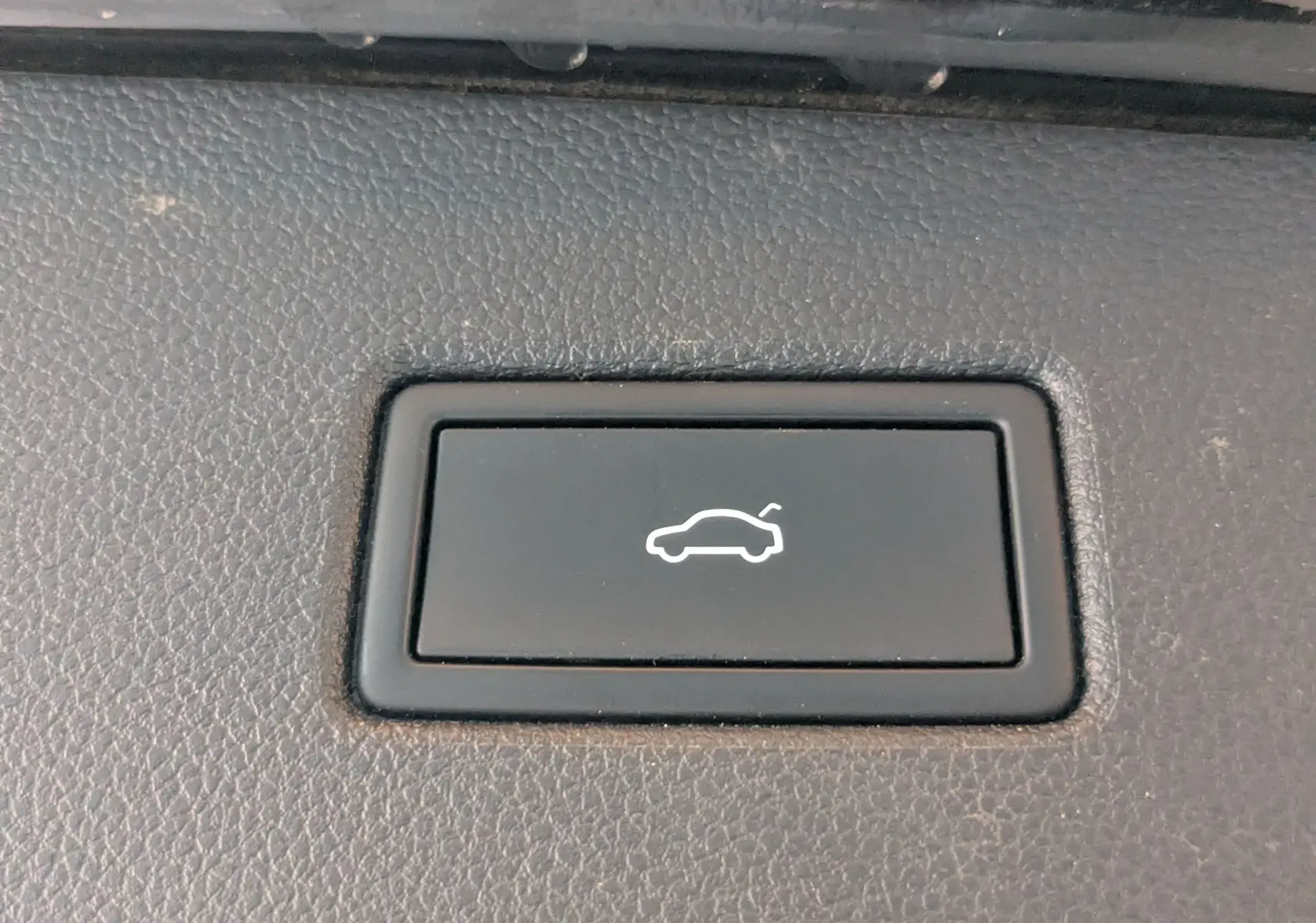 Bouton noir intérieur avec icône blanche d'ouverture de coffre, sur tableau de bord d'un Volkswagen Tiguan noir.