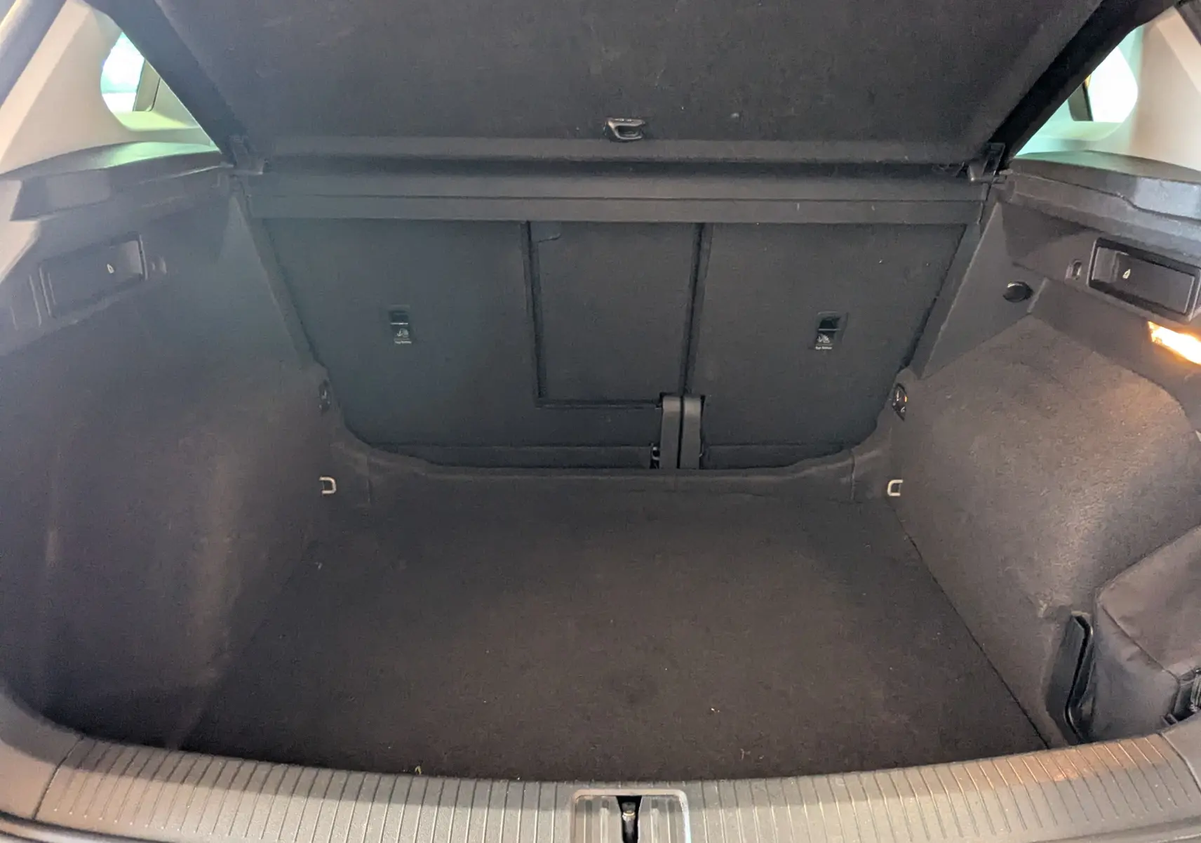 Coffre ouvert en vue arrière d'un Volkswagen Tiguan noir, montrant un espace de chargement vide et bien éclairé.