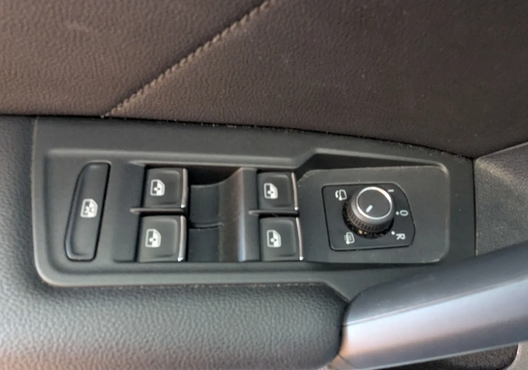 Gros plan sur les commandes de lève-vitres et réglage des rétroviseurs côté conducteur d’un Volkswagen Tiguan noir.