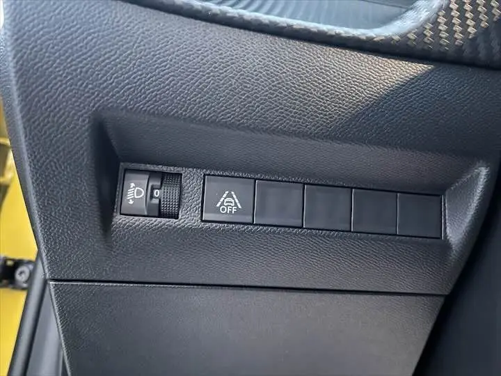 Gros plan sur les commandes de réglage d'éclairage et d'assistance au conducteur côté gauche d'une Peugeot 208 jaune Faro Metal.