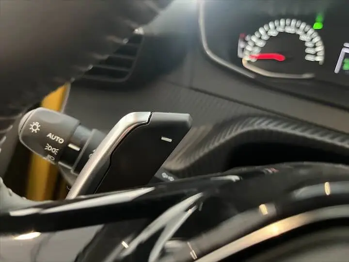 Gros plan sur la commande de boîte automatique et le tableau de bord partiel d’une Peugeot 208 jaune Faro Metal.