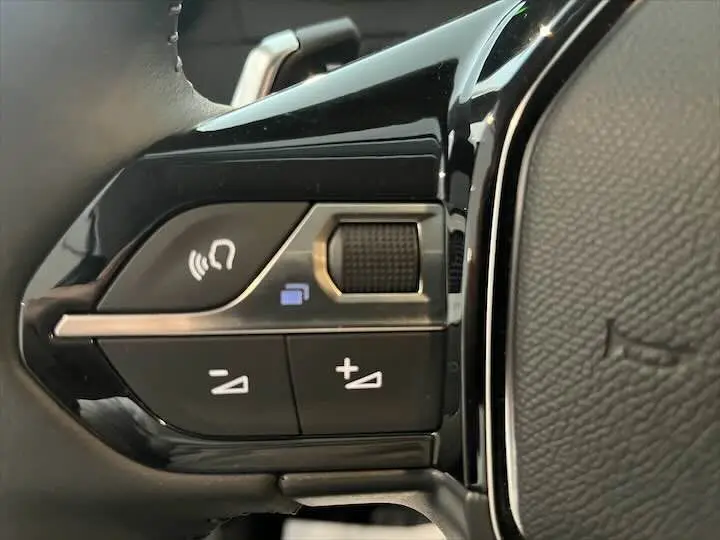 Gros plan sur les commandes de volume et téléphone au volant noir du Peugeot 208 jaune Faro Metal, version 2021.