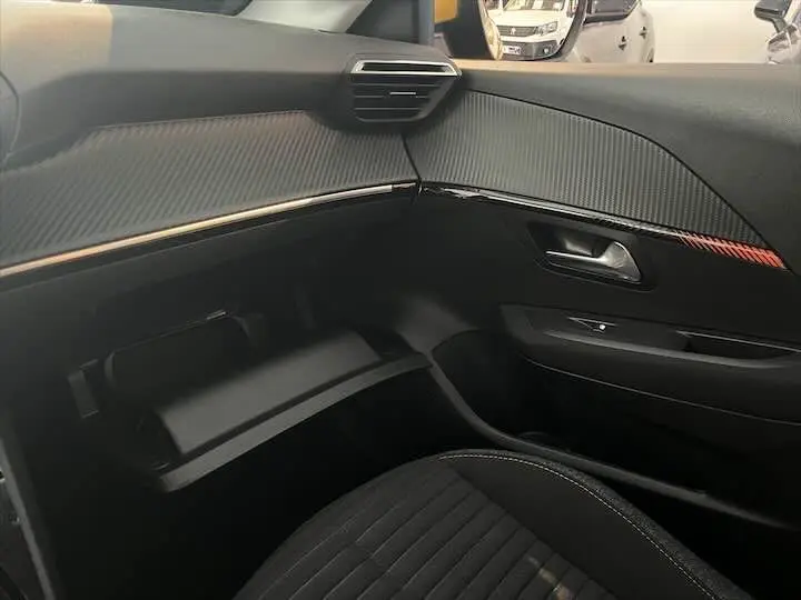 Intérieur de la Peugeot 208 2021, vue côté passager montrant la boîte à gants ouverte et le tableau de bord noir texturé.