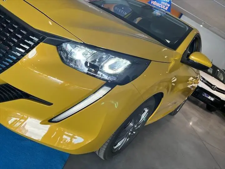 Vue 3/4 avant droite d'une Peugeot 208 jaune Faro Metal avec phares LED allumés en intérieur showroom.