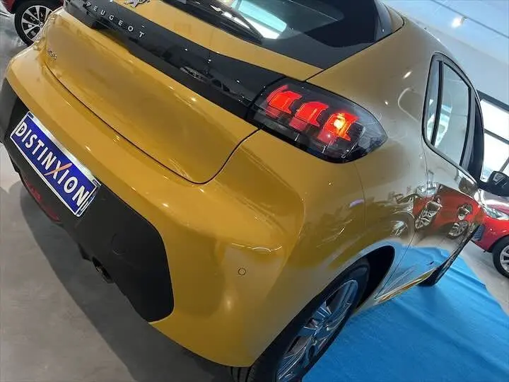 Vue 3/4 arrière droite d'une Peugeot 208 jaune Faro métal avec feux arrière allumés en concession.