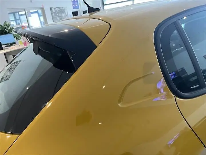 Vue rapprochée du côté arrière gauche d'une Peugeot 208 jaune Faro Métal avec vitre teintée et antenne sur le toit.