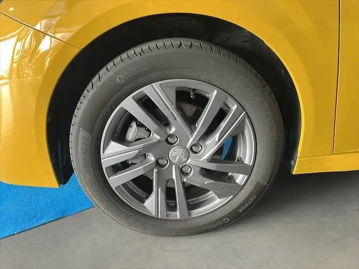 Gros plan sur la roue avant gauche d'une Peugeot 208 jaune Faro Metal avec jante alliage grise et logo Peugeot central.