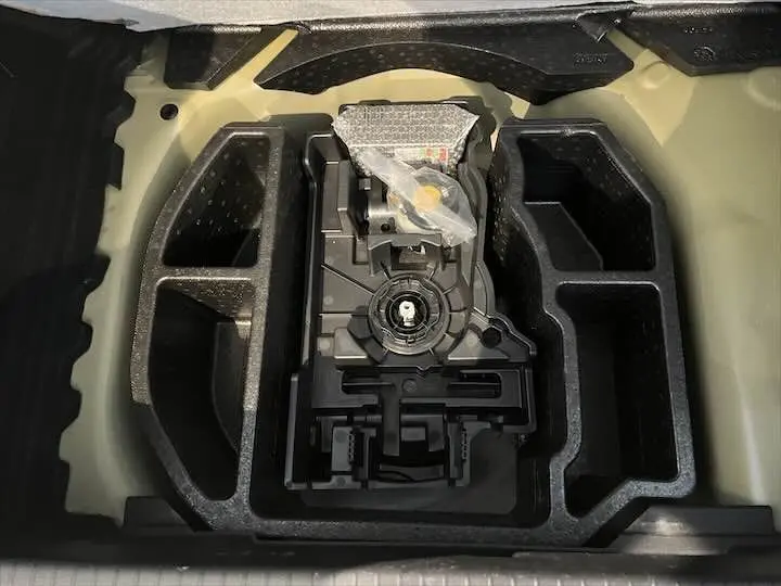 Gros plan sur le rangement en mousse noir du coffre d'une Peugeot 208 jaune Faro Métal, montrant un équipement technique.