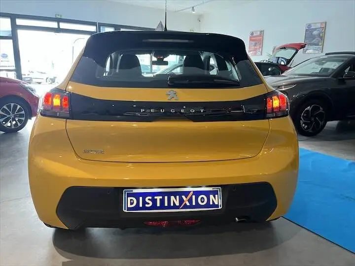 Vue arrière d'une Peugeot 208 jaune Faro Metal en showroom avec feux arrière allumés et plaque Distinxion.