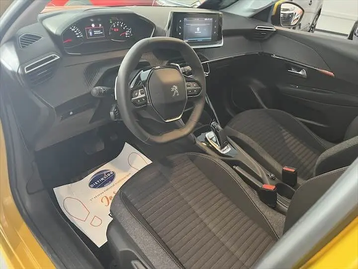 Vue intérieure côté conducteur de la Peugeot 208 jaune Faro Metal, montrant le tableau de bord et les sièges noirs.