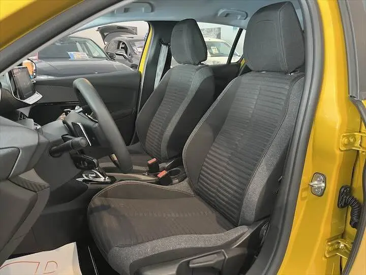 Vue intérieure côté conducteur de la Peugeot 208 jaune Faro Metal, montrant les sièges avant en tissu gris et la console centrale.