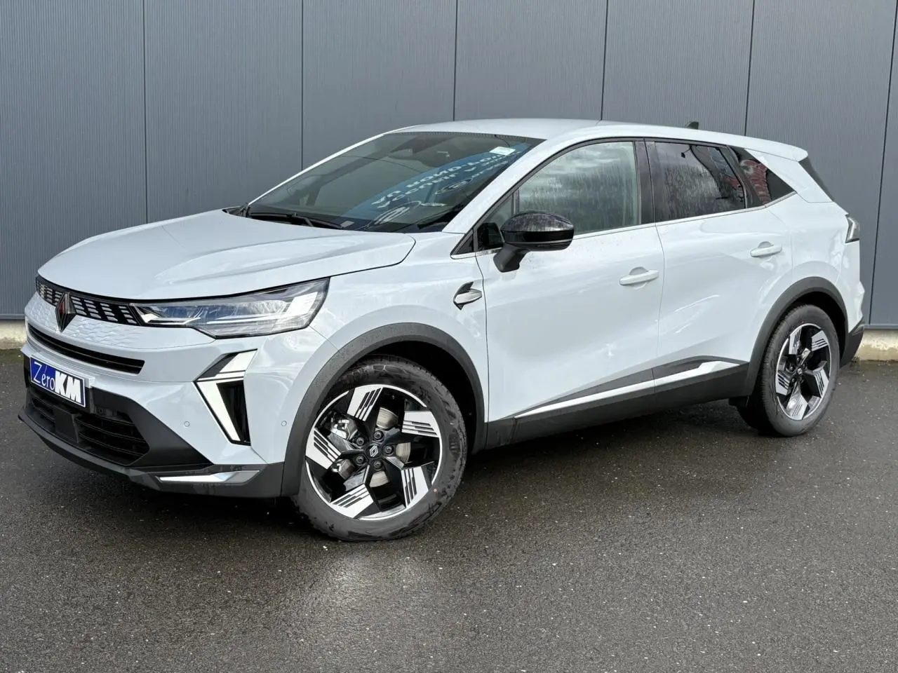 Renault Symbioz gris clair en 3/4 avant droit, avec jantes stylisées et calandre moderne sur fond urbain.