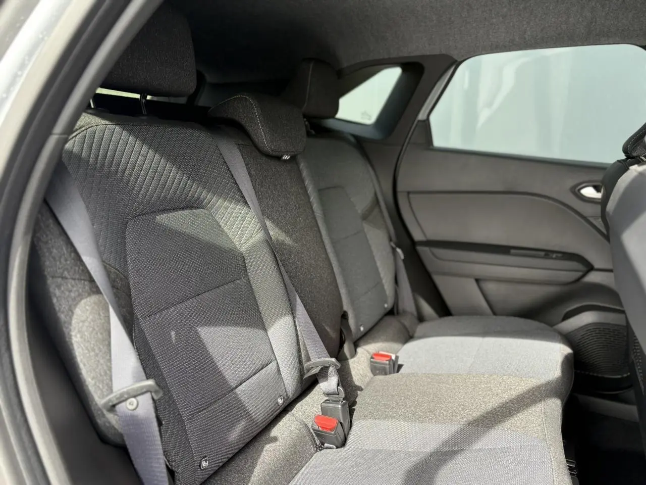 Vue latérale intérieure sur la banquette arrière grise du Renault Symbioz 2025 avec ceintures et appuie-têtes réglables.
