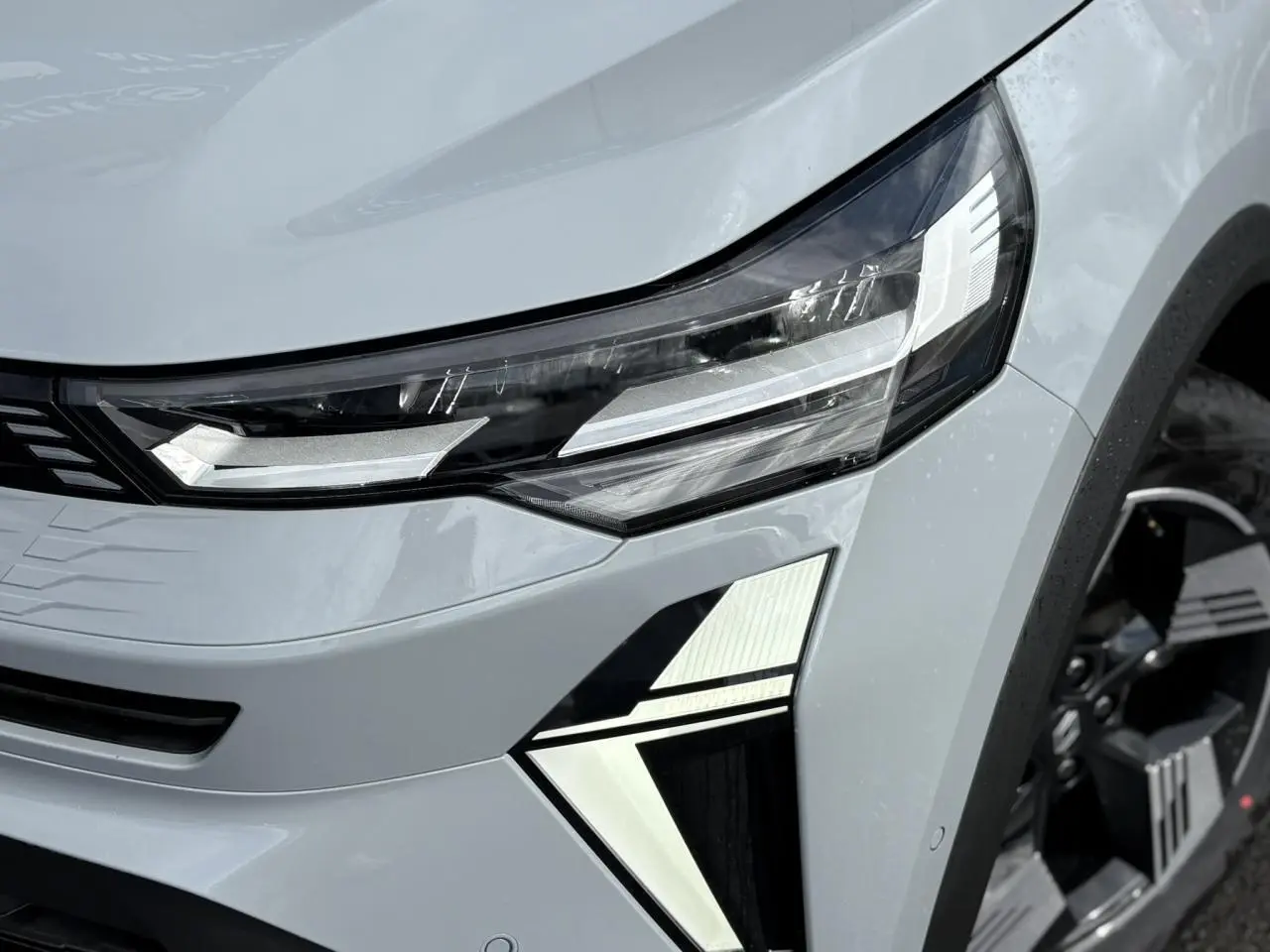 Gros plan sur le phare avant droit et la calandre d'une Renault SYMBIOZ gris clair avec jante noire.