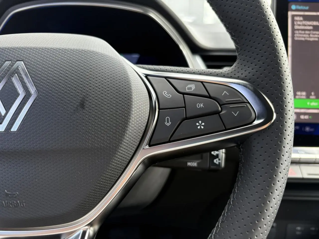 Gros plan sur le volant en cuir perforé de la Renault SYMBIOZ 2025 avec commandes multifonctions et logo central argenté.