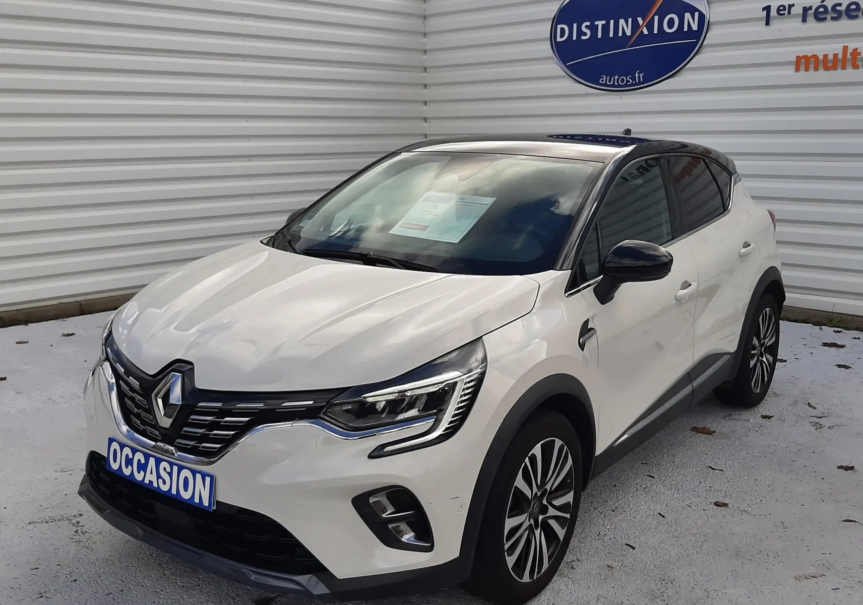 Renault Captur blanc avec toit noir vu de 3/4 avant droit, mettant en valeur ses optiques LED et sa calandre distinctive.
