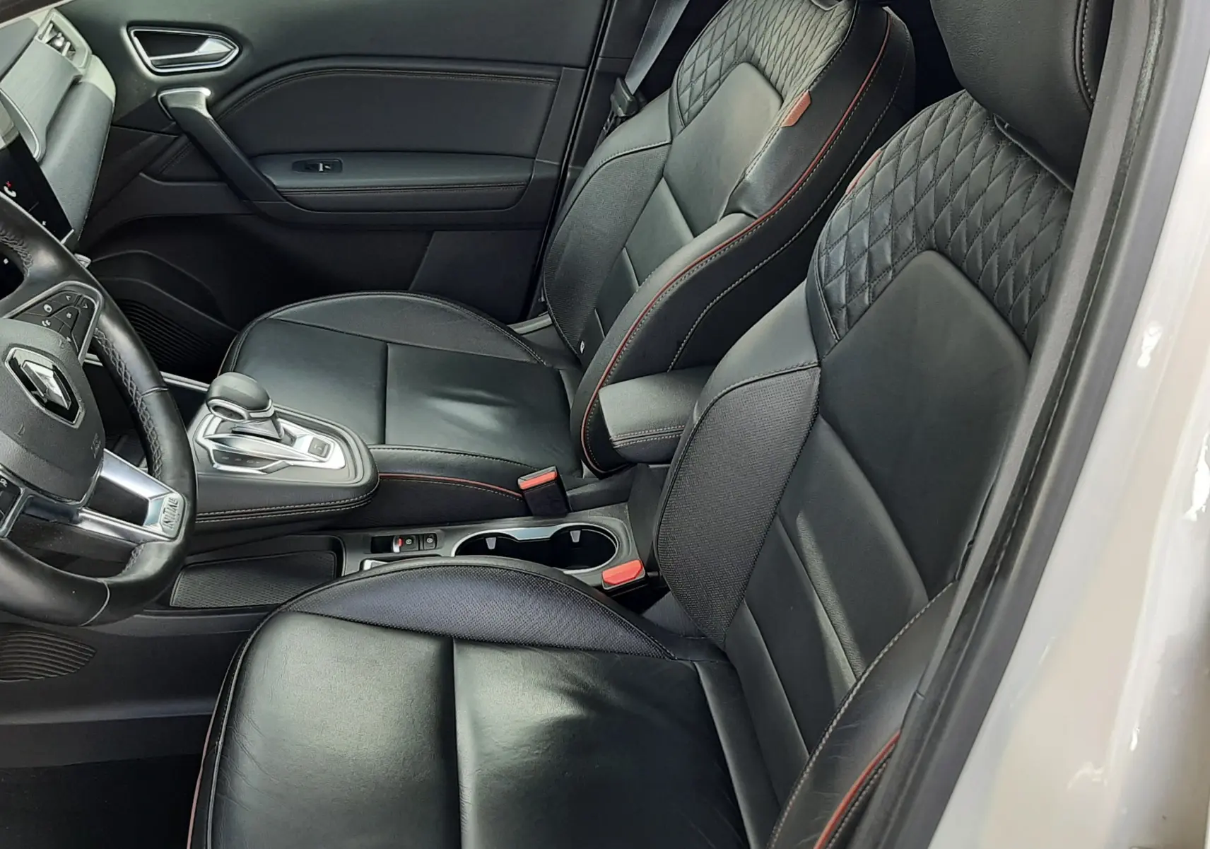 Vue intérieure côté conducteur du Renault Captur blanc toit noir 2020, sièges cuir noirs avec surpiqûres rouges et console centrale.