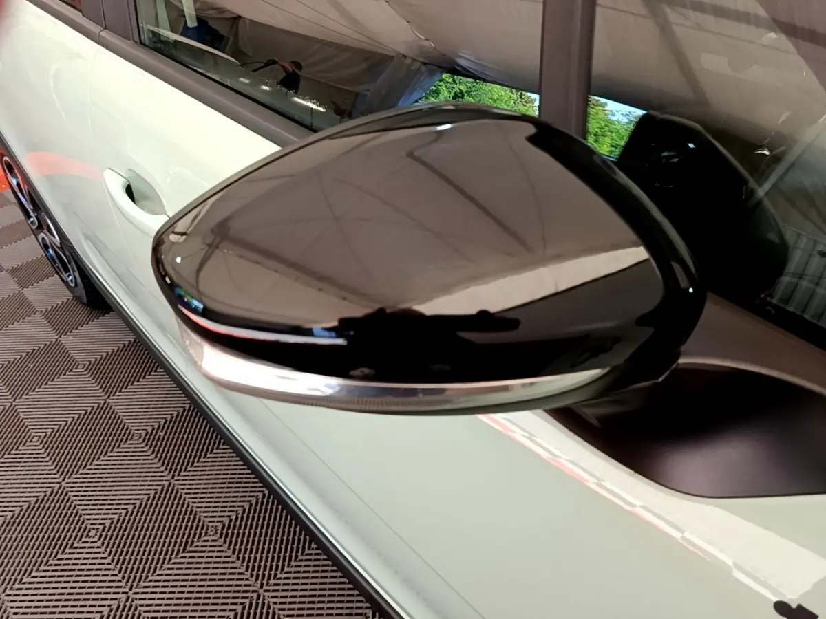 Gros plan sur le rétroviseur droit noir brillant d'une Citroën C3 vert clair, avec poignée de porte visible en arrière-plan.