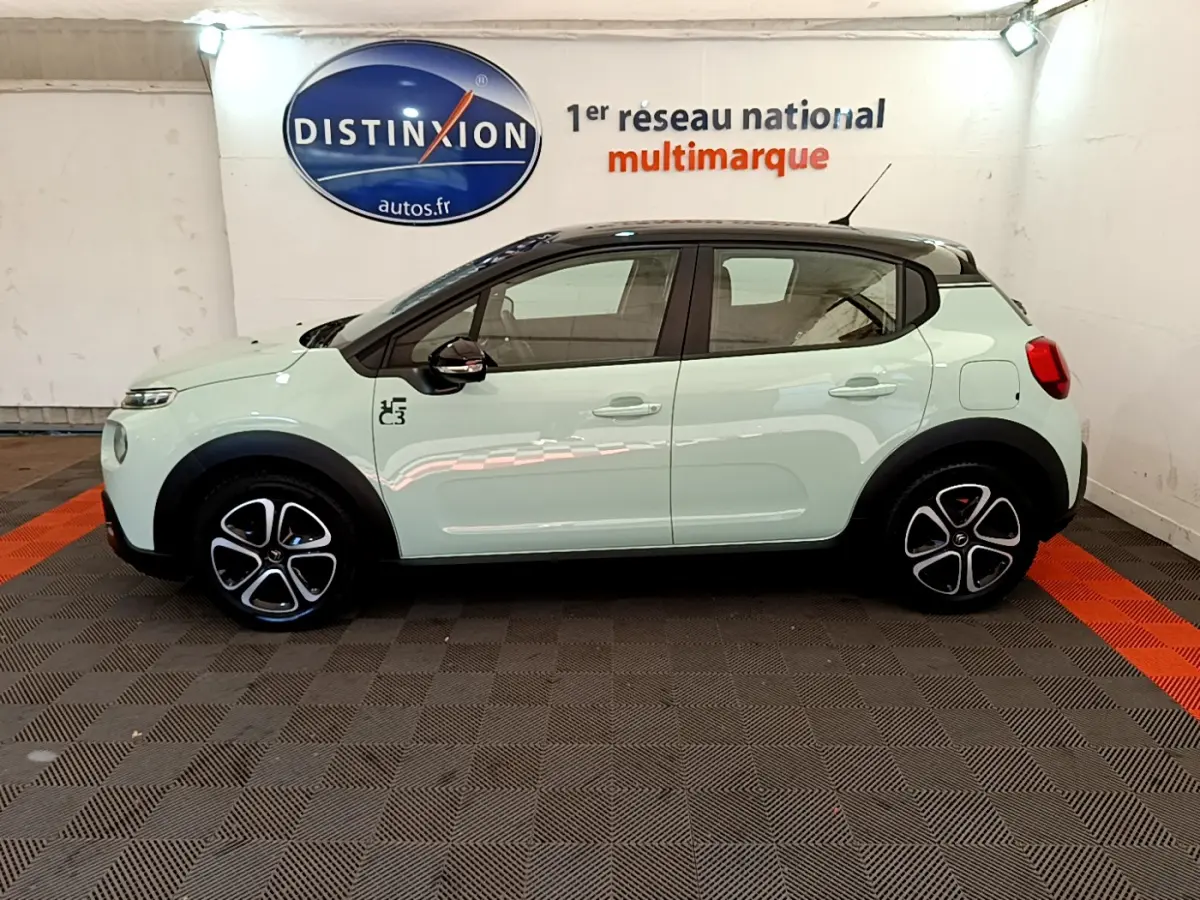 Profil côté gauche d'une Citroën C3 PureTech 82 S&S BVM Graphic vert clair avec toit noir et jantes stylisées en intérieur showroom.