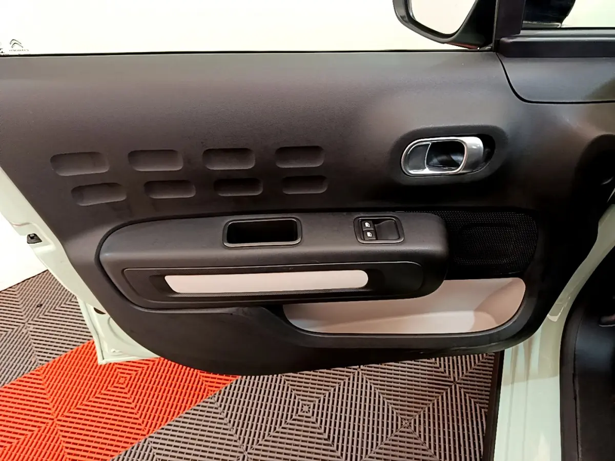 Intérieur côté gauche de la porte d'une Citroën C3 vert clair, avec poignée argentée et commandes de vitres.