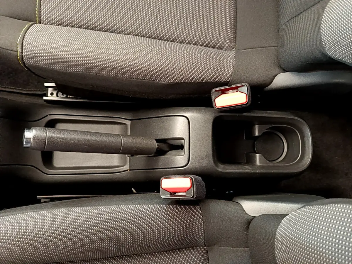Vue plongeante sur la console centrale noire avec frein à main et ceintures rouges de la Citroën C3 verte.