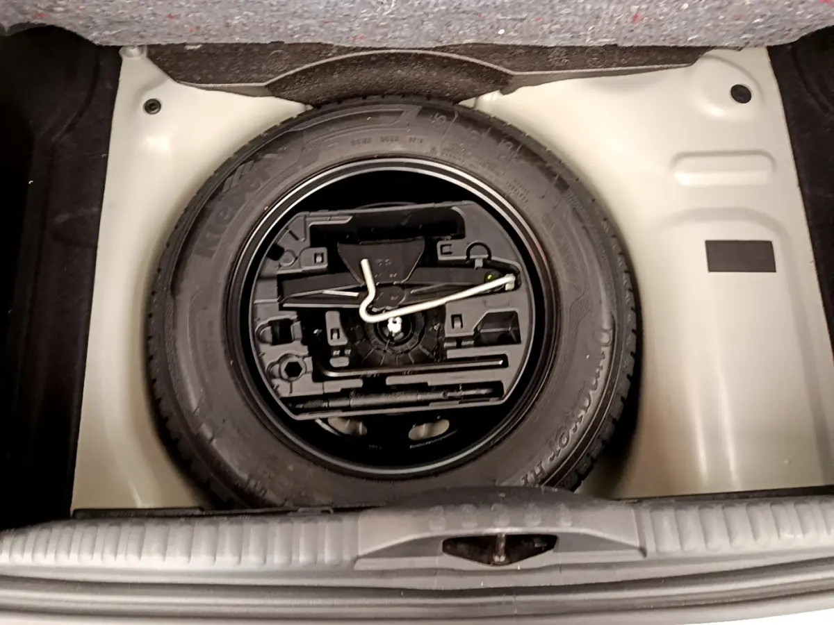 Vue plongeante sur la roue de secours et l'outillage dans le coffre d'une Citroën C3 vert 2019.
