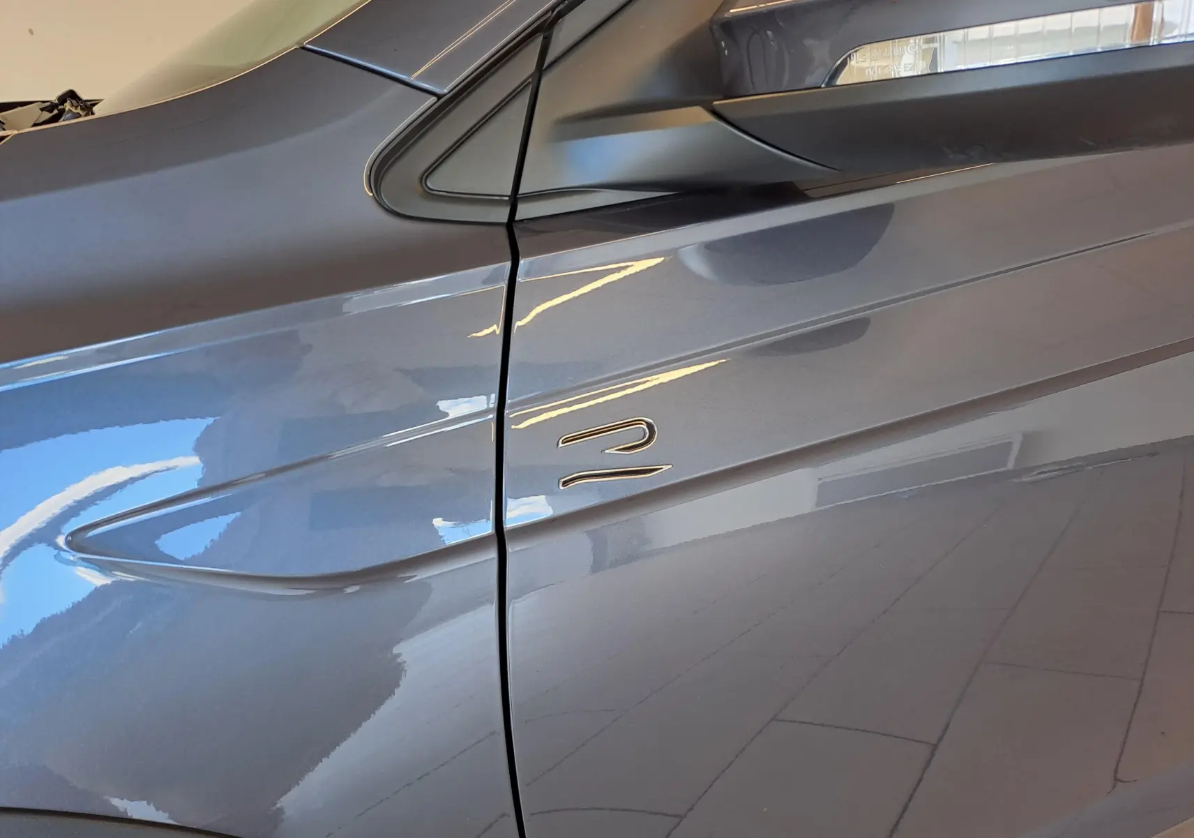 Détail du côté gauche du Volkswagen Taigo gris cendré 2025, mettant en valeur la ligne de caisse et l'emblème R-Line.