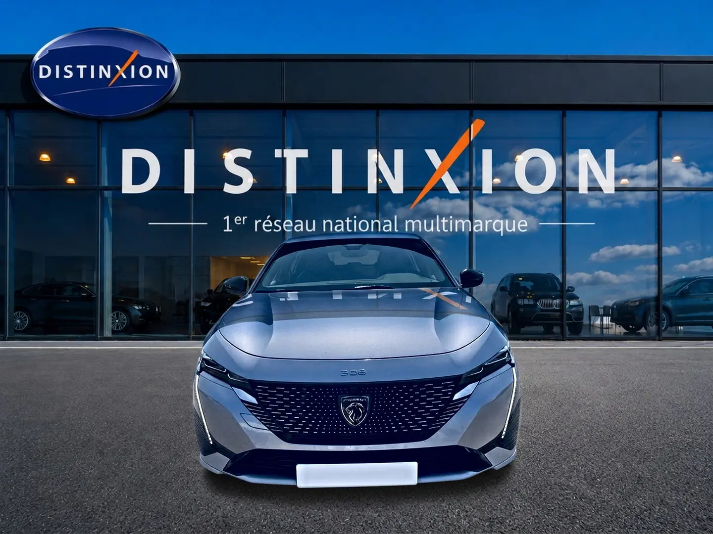 Vue de face d'une Peugeot 308 gris métallisé avec calandre noire et logo lion, devant une vitrine Distinxion.