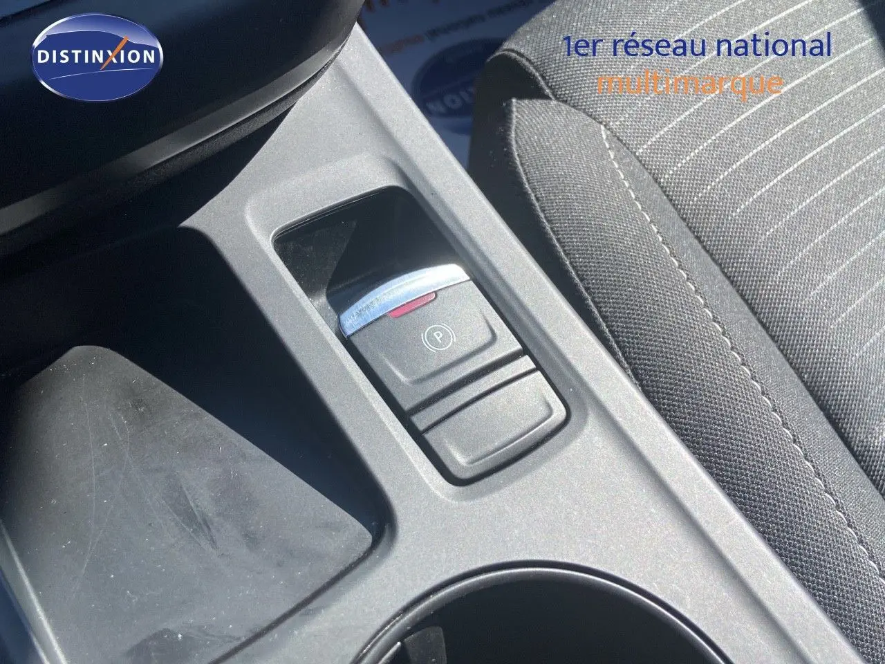 Gros plan sur la console centrale avec frein à main électrique et tissu gris noir du siège d’une Renault Arkana noire.