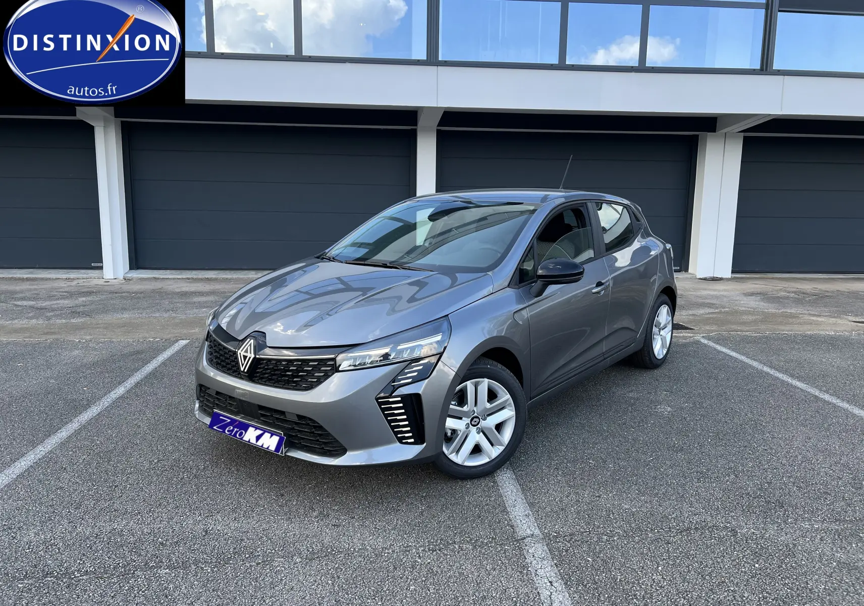 Renault Clio V gris schiste vue 3/4 avant droit, avec jantes alliage et feux LED distinctifs sur parking.