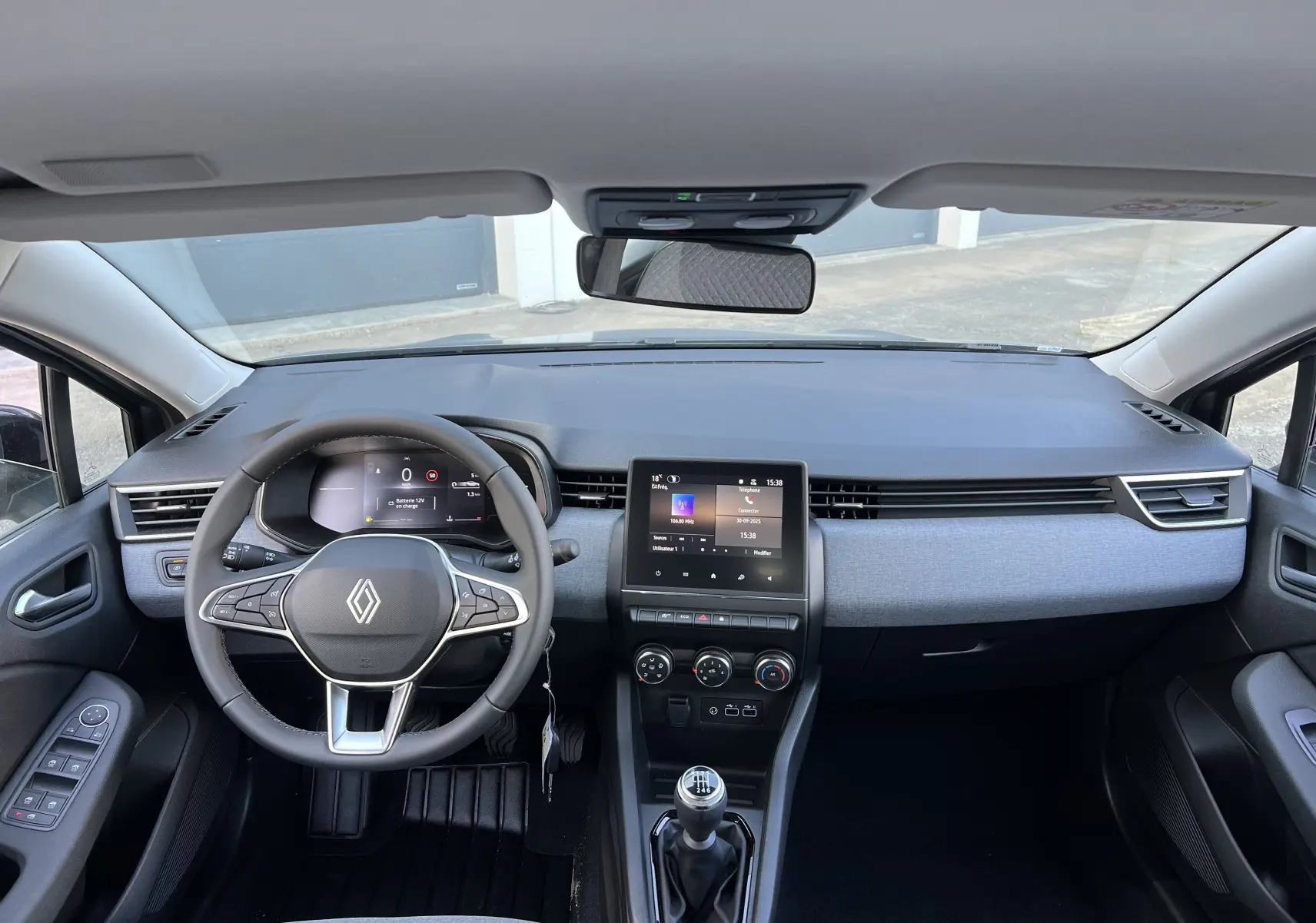 Vue intérieure frontale du tableau de bord et volant de la Renault Clio V gris schiste avec écran tactile 7 pouces et boîte manuelle.