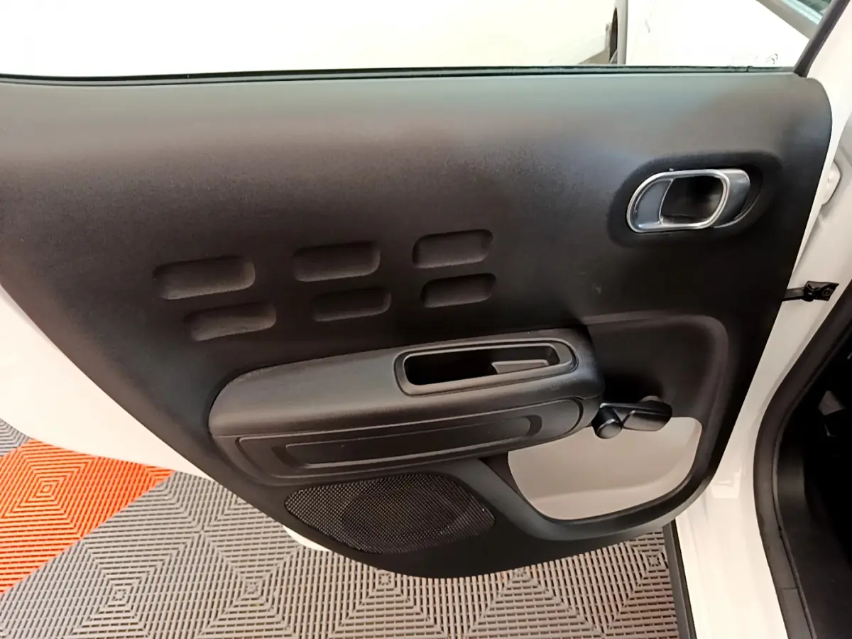 Vue rapprochée de la porte arrière droite blanche de la Citroën C3 2019 avec poignée intérieure noire et manivelle de vitre.