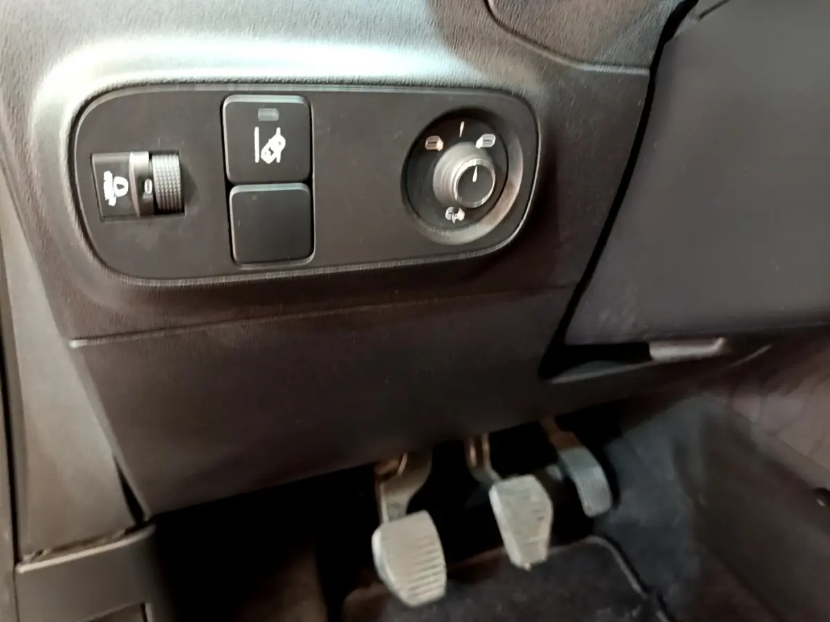 Vue rapprochée côté gauche du poste de conduite de la Citroën C3 blanche, avec commandes et pédales manuelles visibles.