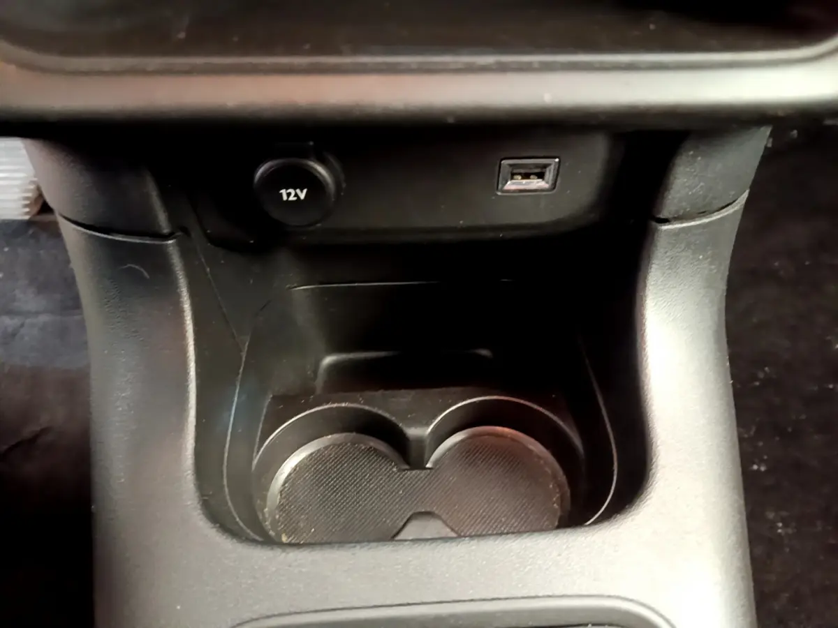 Gros plan sur la console centrale noire de la Citroën C3, montrant prise 12V et port USB au-dessus des porte-gobelets.