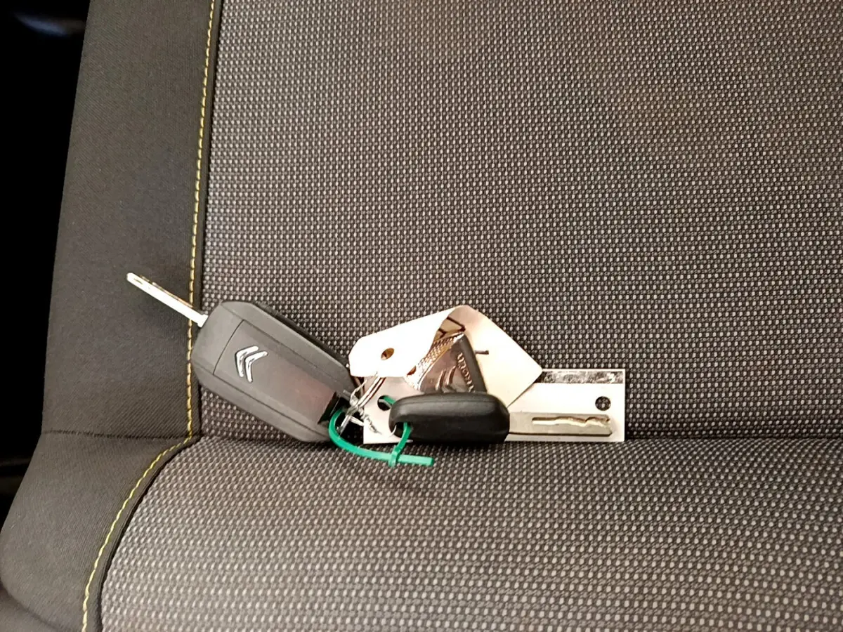 Clé de voiture Citroën posée sur un siège tissu gris foncé avec surpiqûres jaunes visibles.