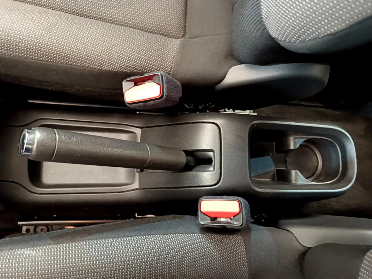 Vue plongeante sur la console centrale noire de la Citroën C3 avec frein à main manuel et ceintures de sécurité rouges.