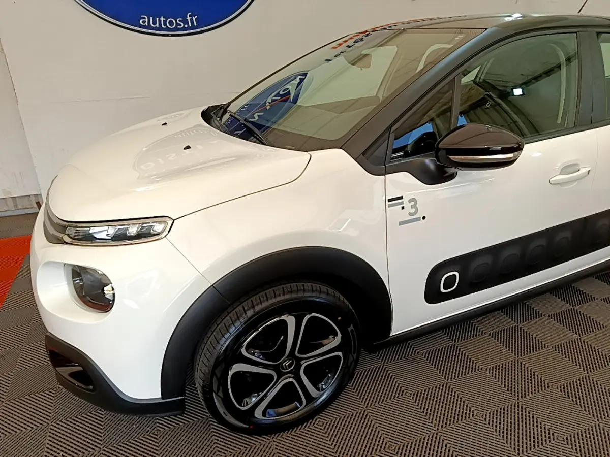 Vue 3/4 avant gauche d'une Citroën C3 blanche avec protections latérales noires et jantes noires distinctives.