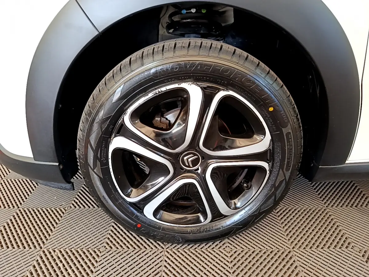 Gros plan sur la roue arrière droite d'une Citroën C3 blanche avec passage de roue noir mat et jante alliage.