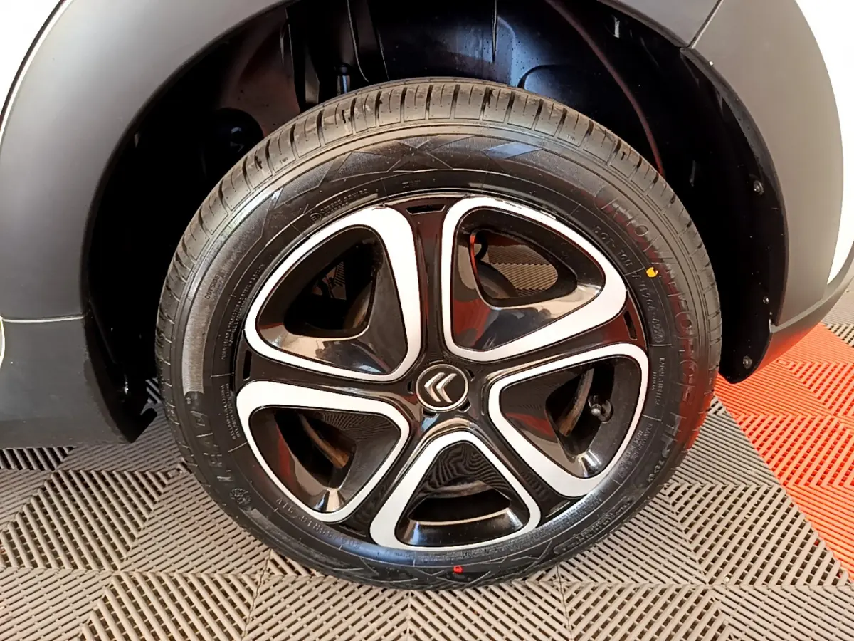 Gros plan sur la roue arrière droite d'une Citroën C3 blanche, avec passage de roue noir et sol carrelé rouge et gris.